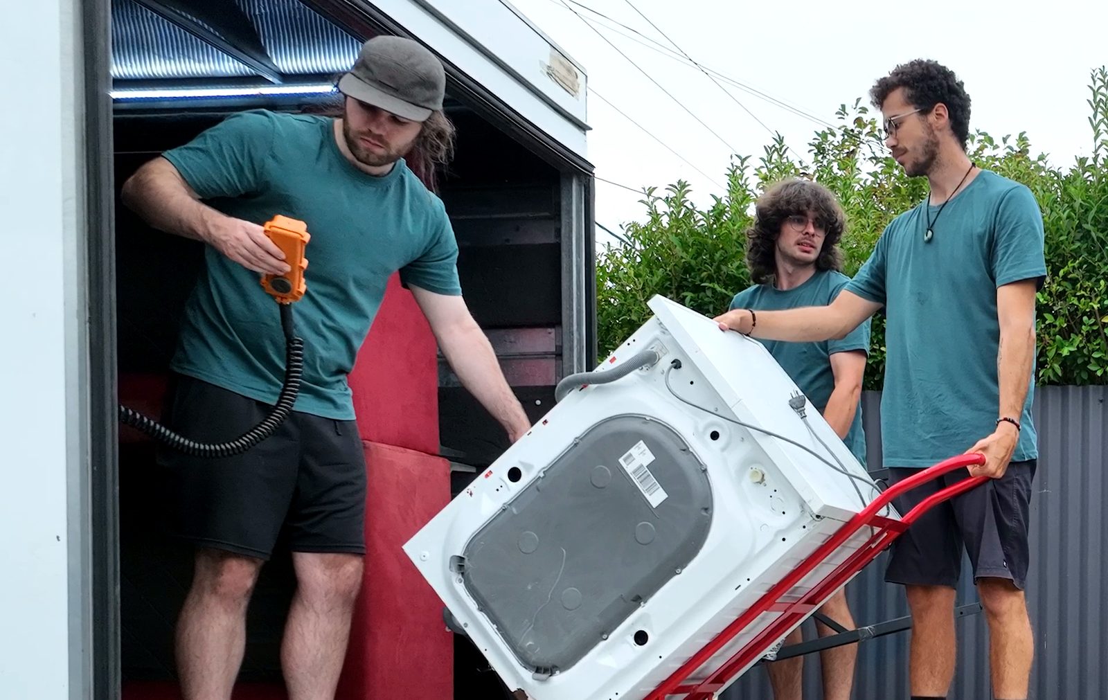 Three movers guide a washing machine on a hand trolley